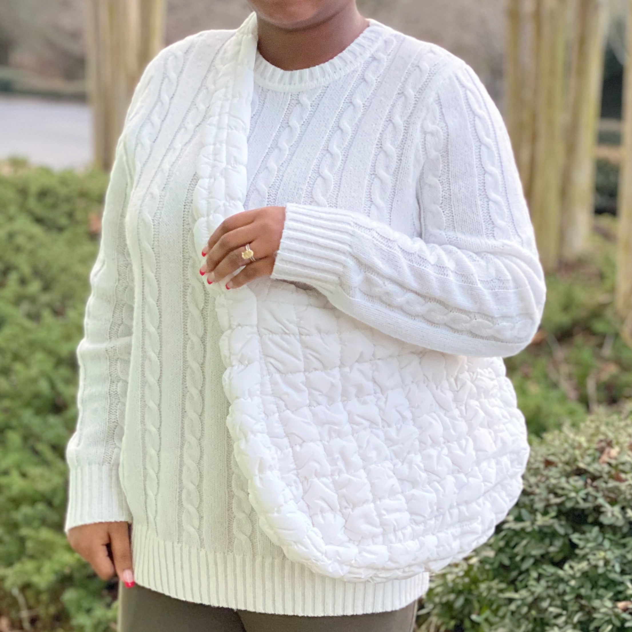 Woman holding a Carry All Quilted Cross Body Bag while wearing a cozy white sweater.