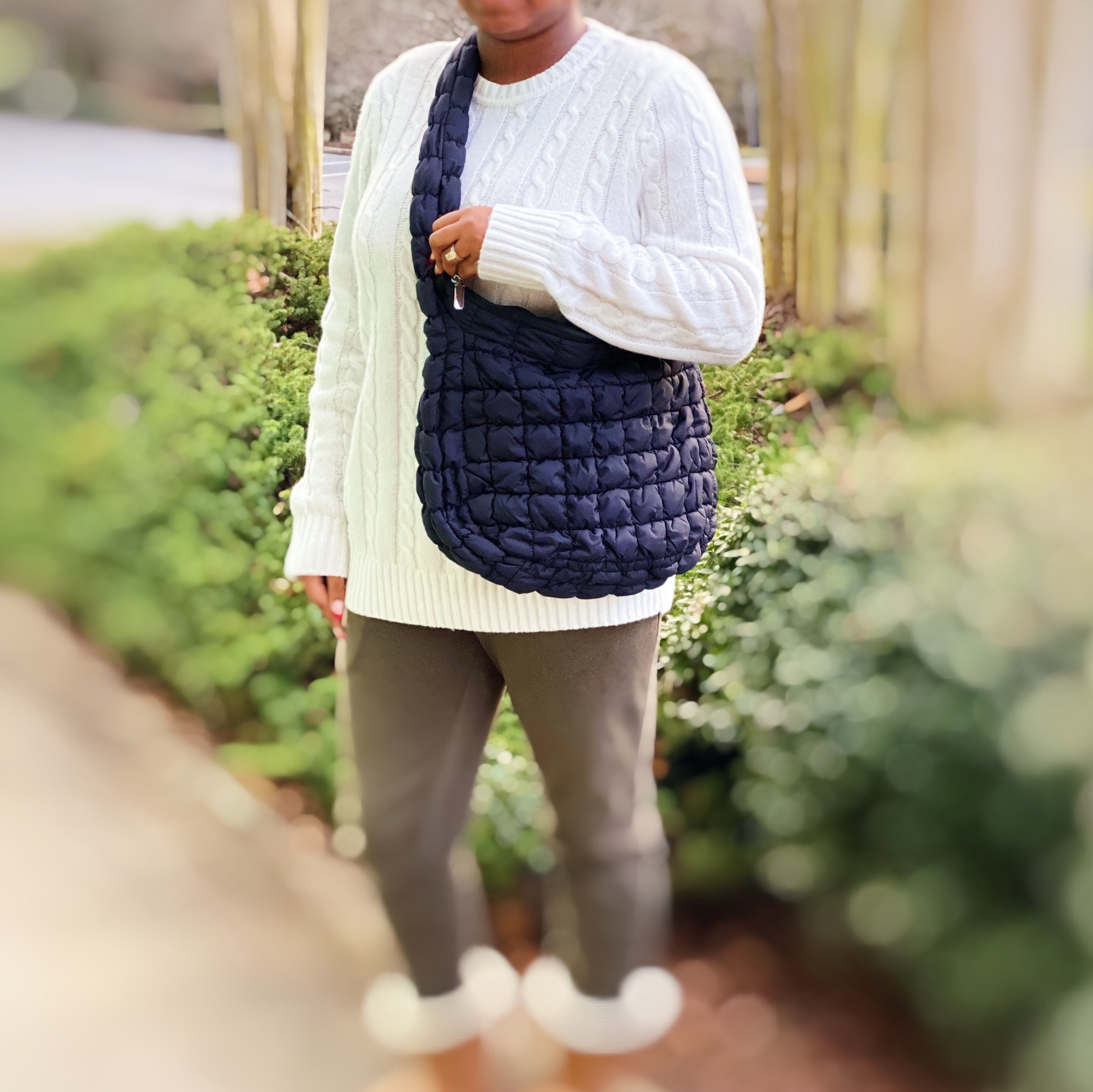 Woman holding a Carry All Quilted Cross Body Bag while wearing a cozy white sweater.