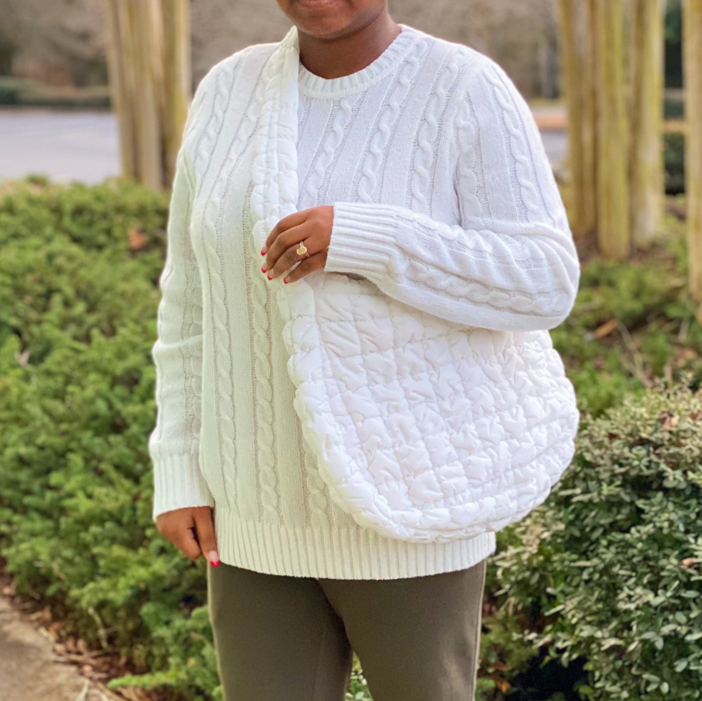Woman holding a Carry All Quilted Cross Body Bag while wearing a cozy white sweater.